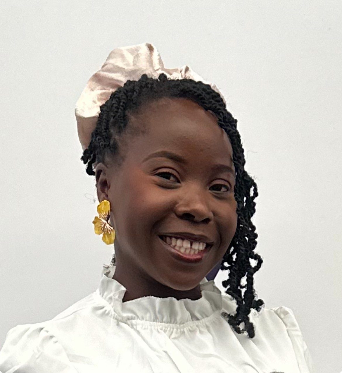 A woman is looking at the camera and smiling. She is wearing a white top.