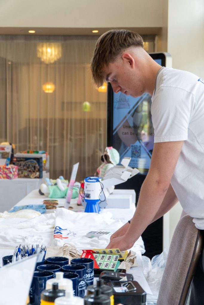 A man is stood behind a fundraising table and he is sorting through raffle tickets.