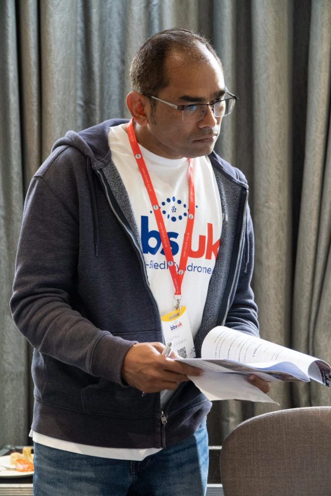 A man is stood wearing a BBS UK tshirt and holding sheets of paper.