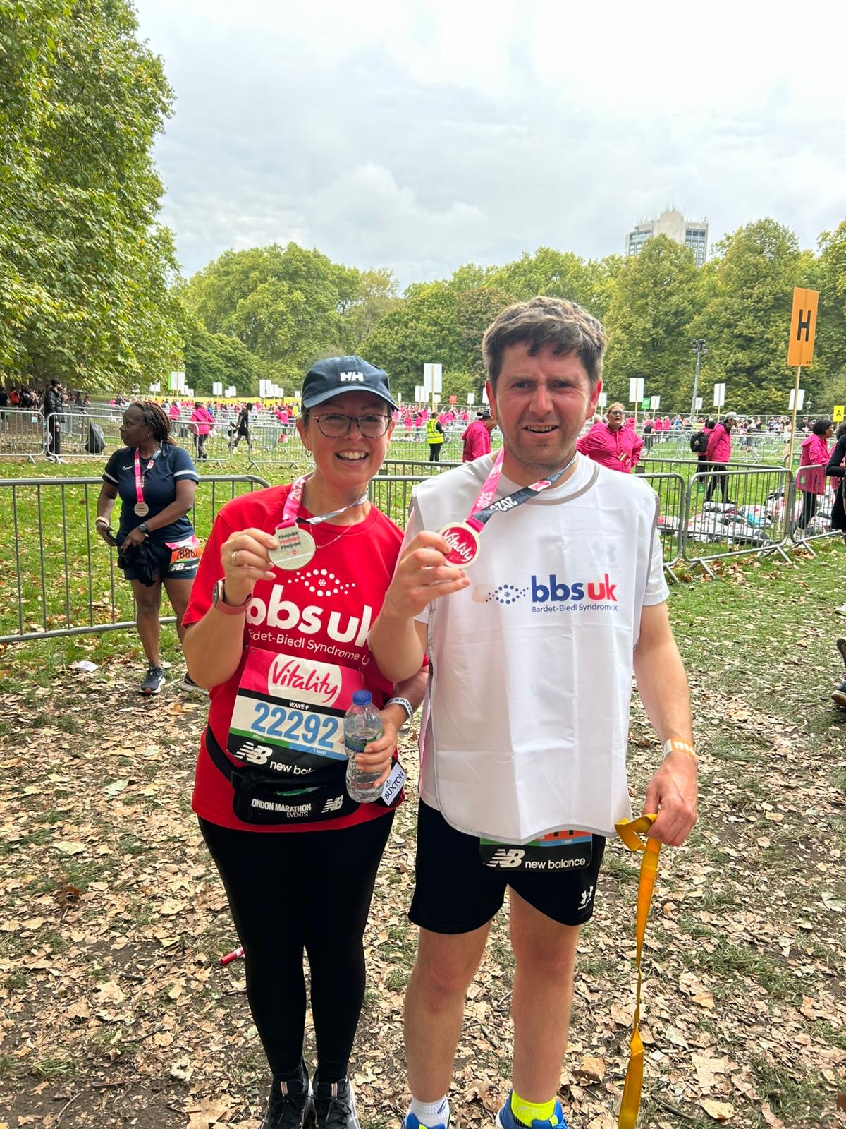 A man and a woman are wearing BBS UK t-shirts and are holding up medals after completing a race.