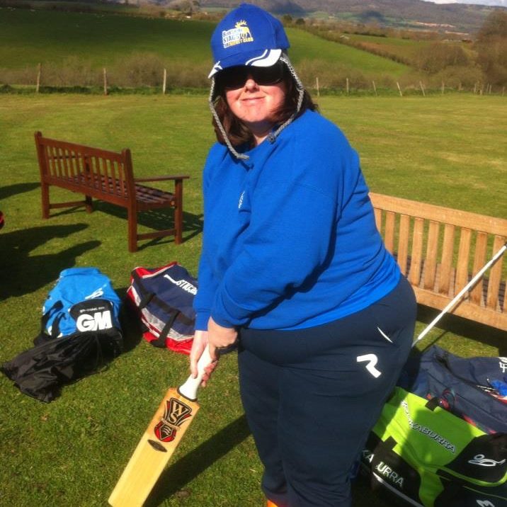 A woman is holding a cricket bat and stood in a field.