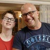 A man and a teenage boy are stood next to each other and similing.