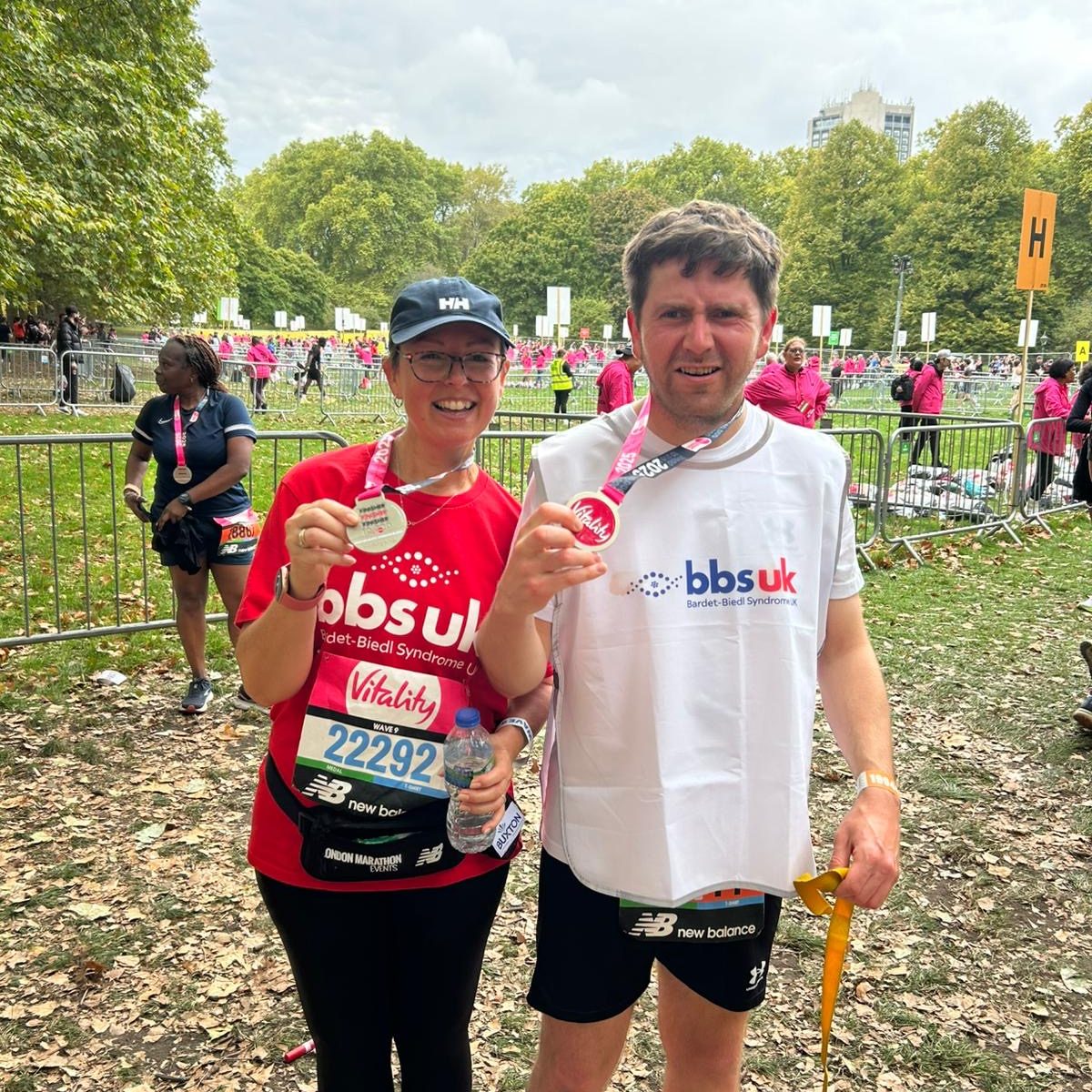 A man and a woman are wearing BBS UK t-shirts and are holding up medals after completing a race.