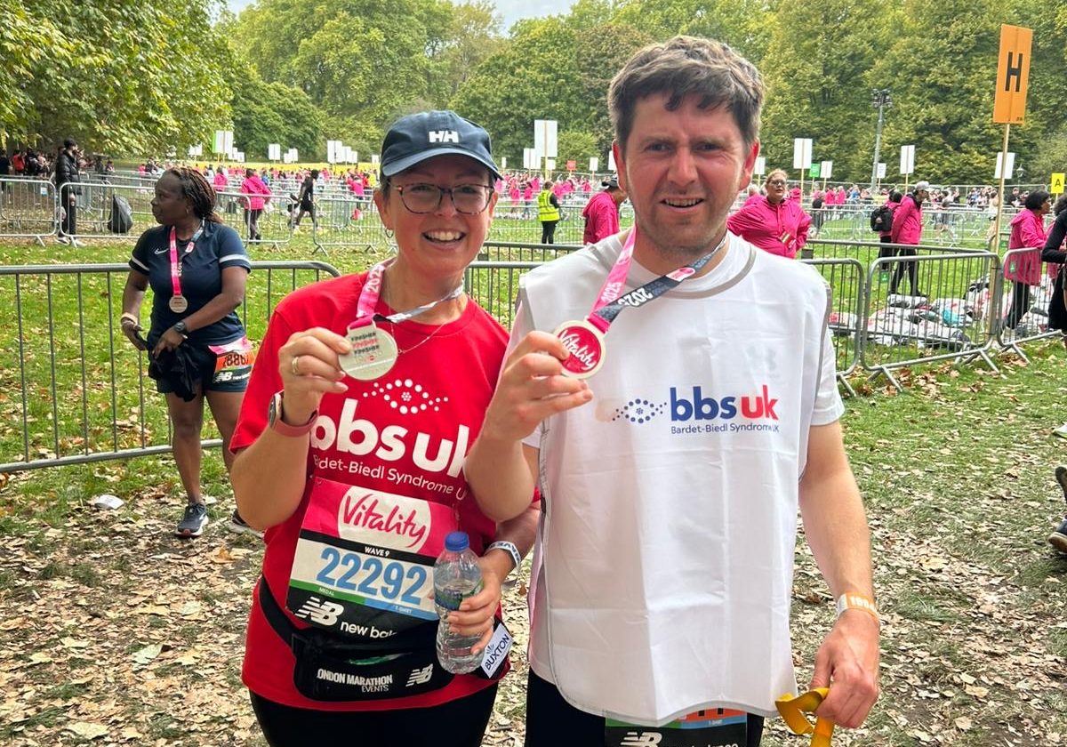 A man and a woman are wearing BBS UK t-shirts and are holding up medals after completing a race.