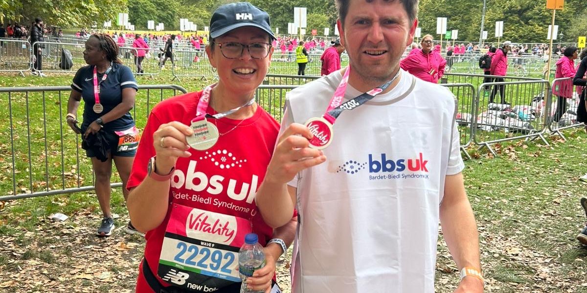 A man and a woman are wearing BBS UK t-shirts and are holding up medals after completing a race.